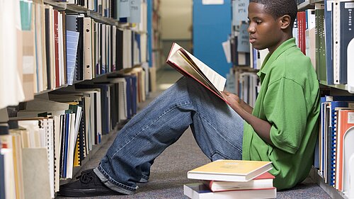 A child sitting on the floor in a library reading a book.